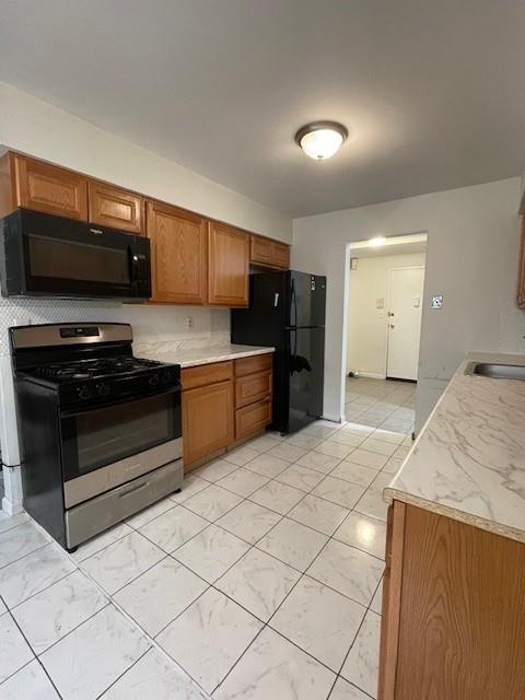 kitchen featuring brown cabinetry, light countertops, a sink, and black appliances