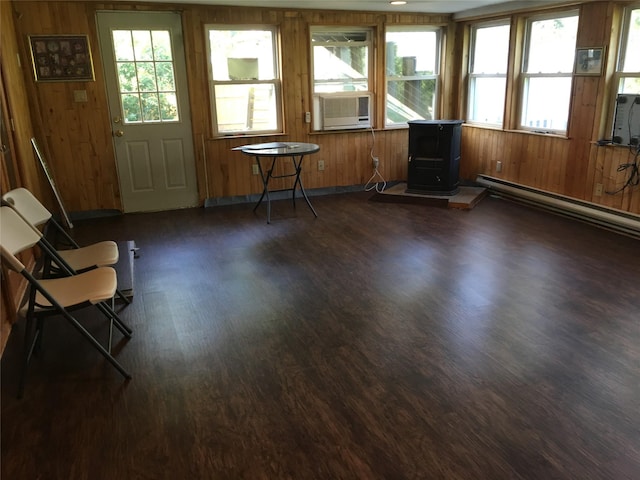 unfurnished sunroom featuring a wood stove, cooling unit, a baseboard heating unit, and a wealth of natural light