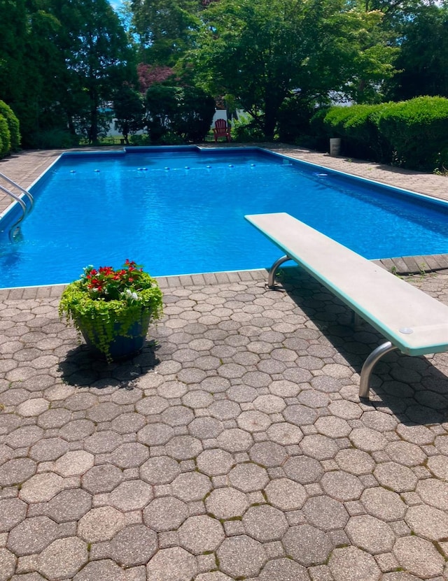 outdoor pool with a diving board and a patio