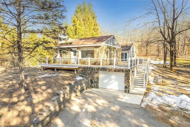 view of home's exterior featuring driveway, stone siding, stairway, an attached garage, and a deck