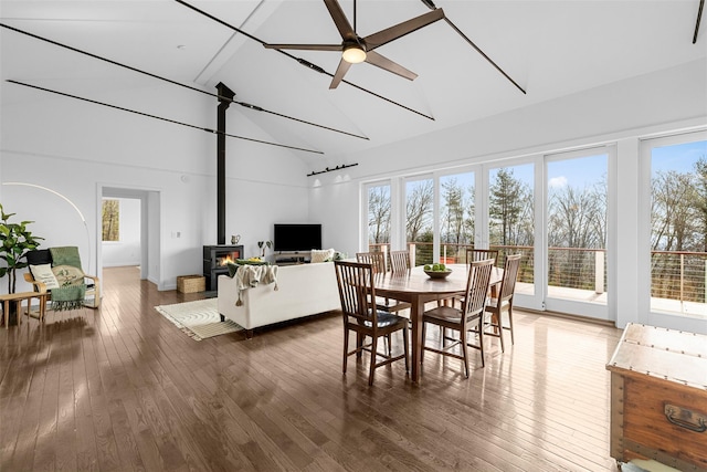 dining room featuring a wood stove, a ceiling fan, high vaulted ceiling, and hardwood / wood-style floors