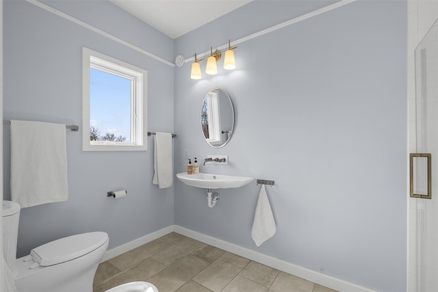 bathroom with tiled shower, a sink, toilet, and baseboards