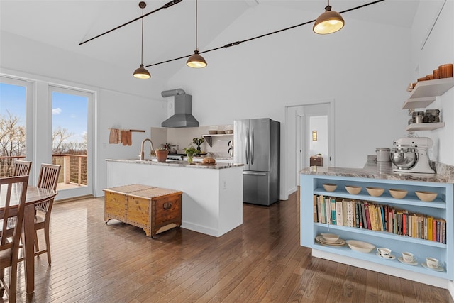 kitchen featuring dark wood finished floors, open shelves, hanging light fixtures, freestanding refrigerator, and wall chimney range hood