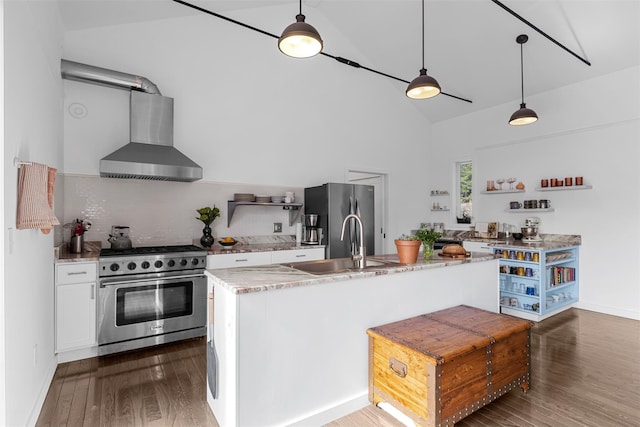 kitchen featuring open shelves, stainless steel appliances, a sink, wall chimney range hood, and wood finished floors