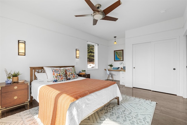 bedroom with ceiling fan, a closet, built in desk, and wood finished floors