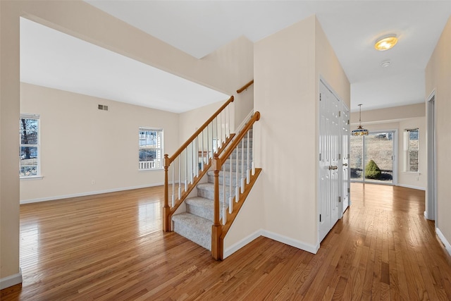 stairway with a wealth of natural light, wood-type flooring, visible vents, and baseboards