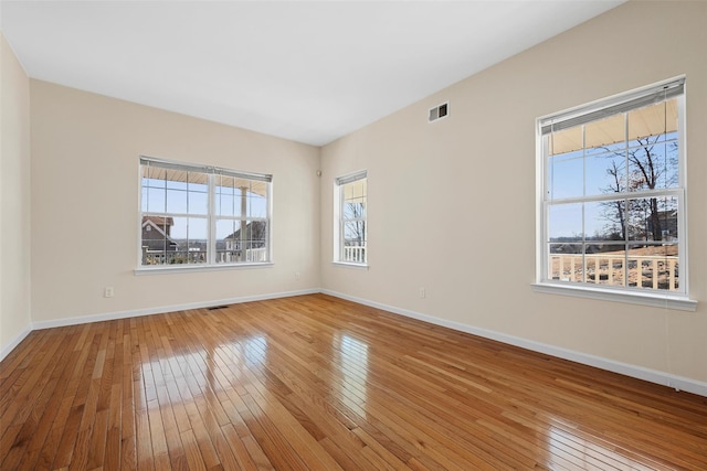 empty room featuring hardwood / wood-style floors, visible vents, and baseboards