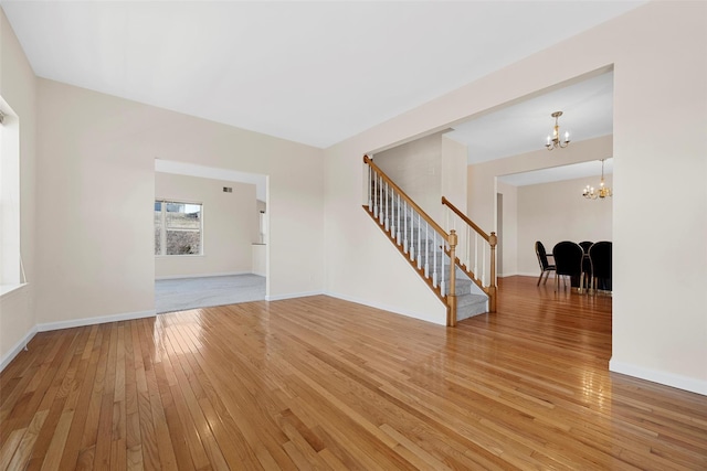 unfurnished room featuring light wood-type flooring, stairway, baseboards, and a chandelier