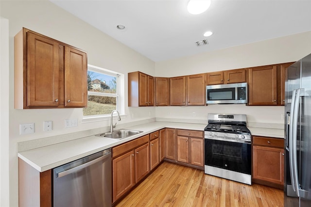 kitchen featuring visible vents, brown cabinets, stainless steel appliances, light wood-type flooring, and a sink