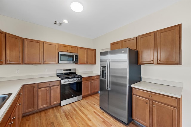 kitchen with light wood finished floors, appliances with stainless steel finishes, brown cabinets, and light countertops