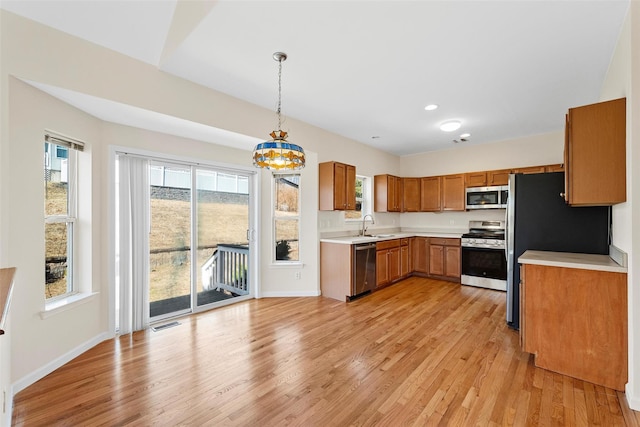 kitchen featuring brown cabinets, light wood finished floors, stainless steel appliances, light countertops, and a sink