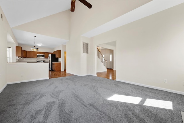 unfurnished living room with dark colored carpet, visible vents, stairway, a sink, and baseboards