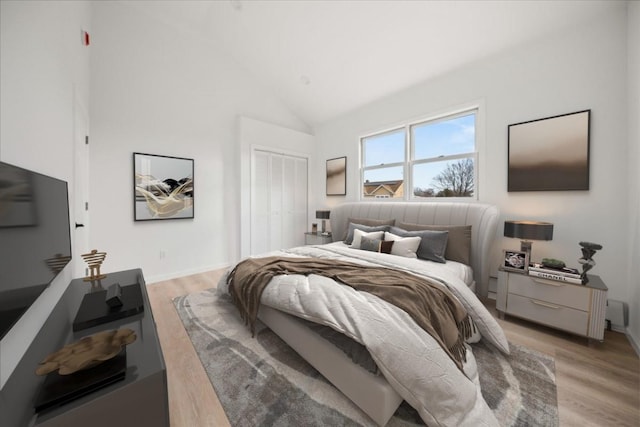 bedroom with high vaulted ceiling, a closet, light wood-style flooring, and baseboards