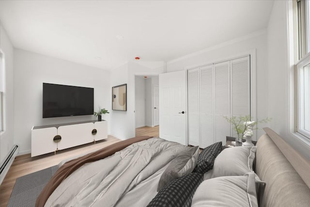 bedroom with a baseboard heating unit, a closet, wood finished floors, and baseboards