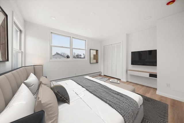 bedroom with a baseboard radiator, a closet, baseboards, and wood finished floors