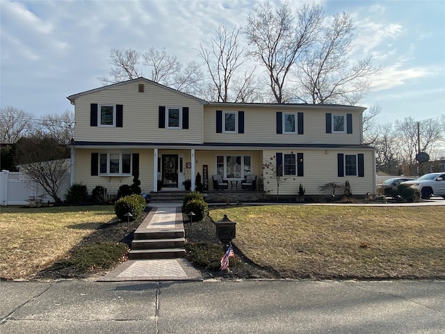 view of front of home with covered porch, fence, and a front yard