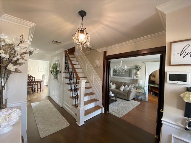 staircase with wood finished floors, visible vents, crown molding, and an inviting chandelier