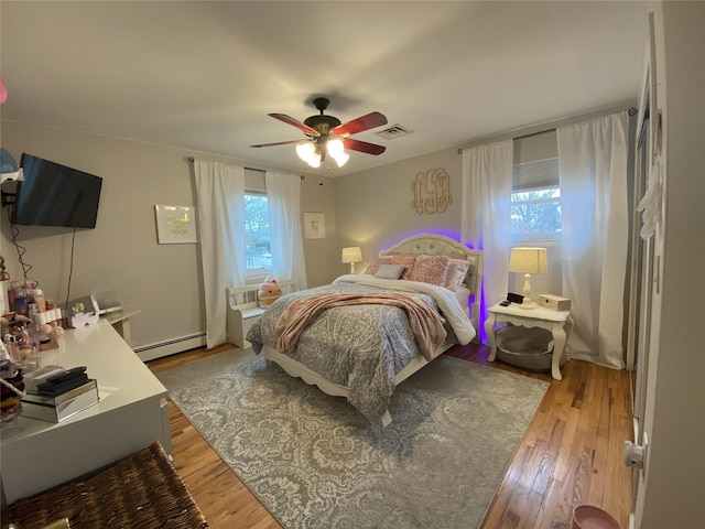 bedroom featuring ceiling fan, a baseboard heating unit, light wood-style flooring, and visible vents