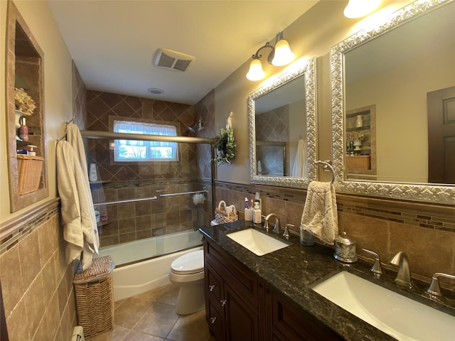 bathroom with toilet, tile walls, a sink, and visible vents