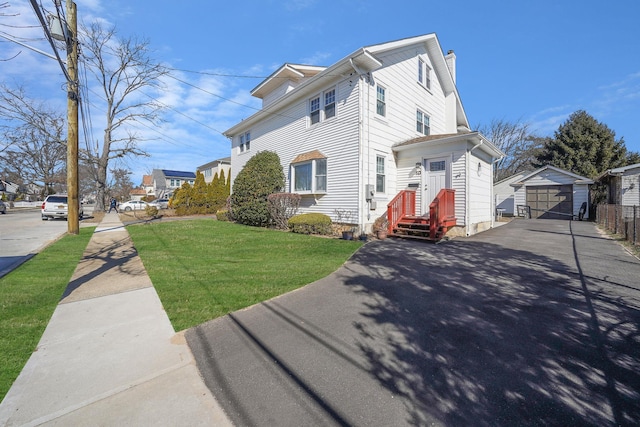 view of front facade featuring aphalt driveway, a storage unit, a front yard, a garage, and an outdoor structure