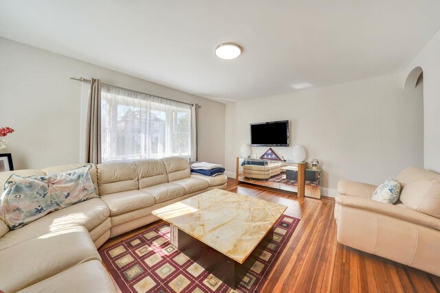 living area featuring arched walkways, baseboards, and wood finished floors