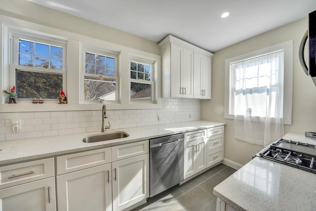 kitchen with light stone counters, a sink, white cabinetry, stainless steel dishwasher, and decorative backsplash