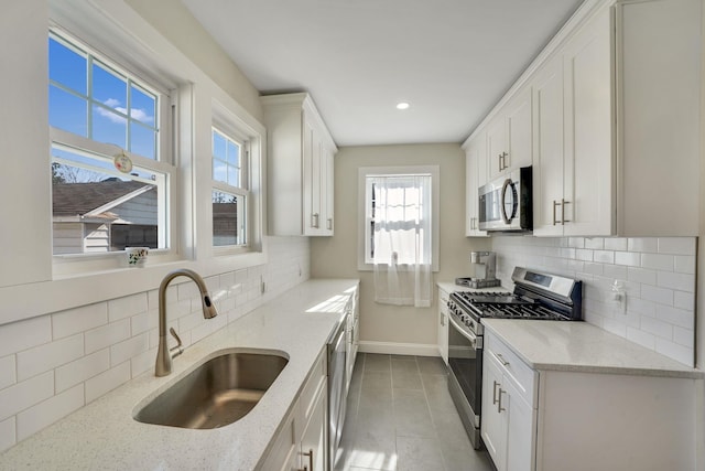 kitchen featuring white cabinetry, appliances with stainless steel finishes, light stone counters, and a sink