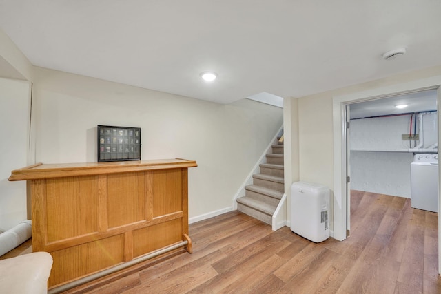 bar featuring a dry bar, light wood finished floors, baseboards, washer / clothes dryer, and stairs