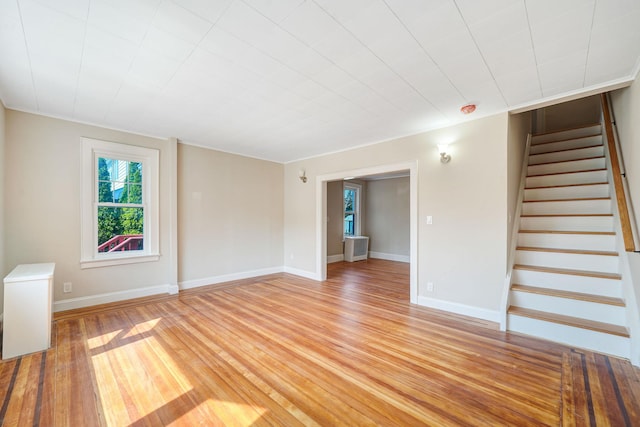 unfurnished living room with baseboards, stairway, and light wood-style floors