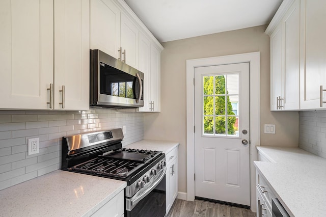 kitchen featuring white cabinets, light stone countertops, stainless steel appliances, and wood finished floors