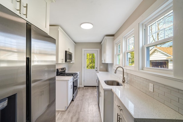 kitchen with light stone counters, a sink, white cabinetry, appliances with stainless steel finishes, and decorative backsplash