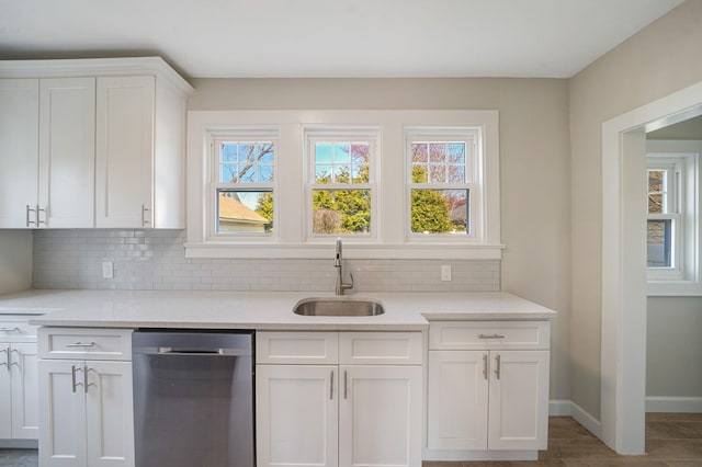 kitchen featuring tasteful backsplash, a wealth of natural light, white cabinets, a sink, and dishwasher