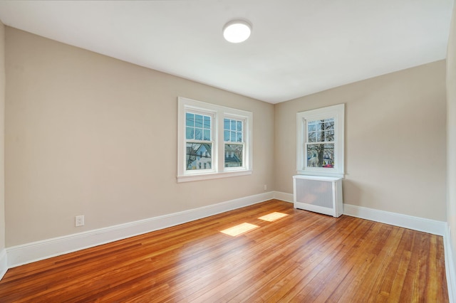 unfurnished room featuring light wood finished floors, radiator heating unit, and baseboards