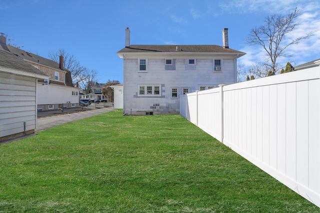 back of house featuring a lawn, a chimney, and fence