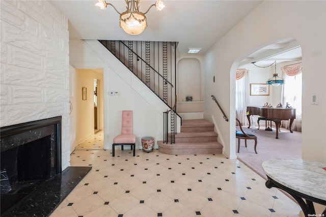 foyer entrance with arched walkways, a notable chandelier, a premium fireplace, visible vents, and stairs