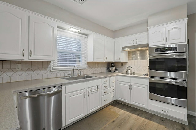 kitchen featuring light wood-style flooring, backsplash, appliances with stainless steel finishes, a sink, and under cabinet range hood