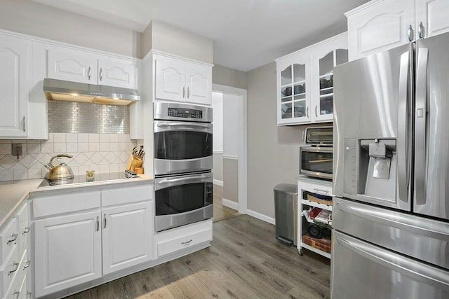 kitchen featuring decorative backsplash, glass insert cabinets, wood finished floors, stainless steel appliances, and under cabinet range hood