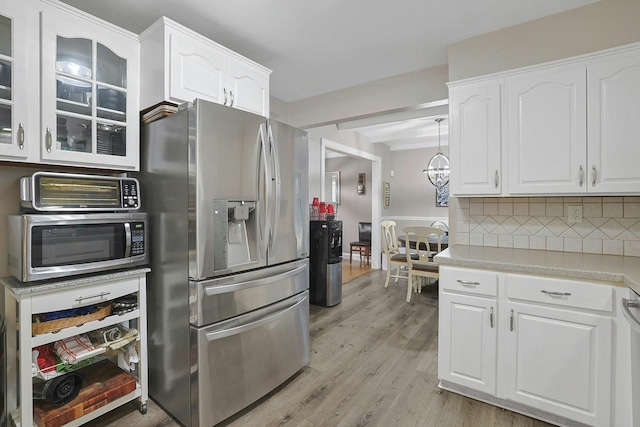 kitchen with light wood finished floors, tasteful backsplash, glass insert cabinets, appliances with stainless steel finishes, and white cabinetry