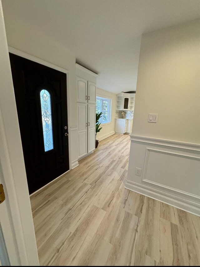 entryway featuring light wood-style flooring, a decorative wall, and wainscoting