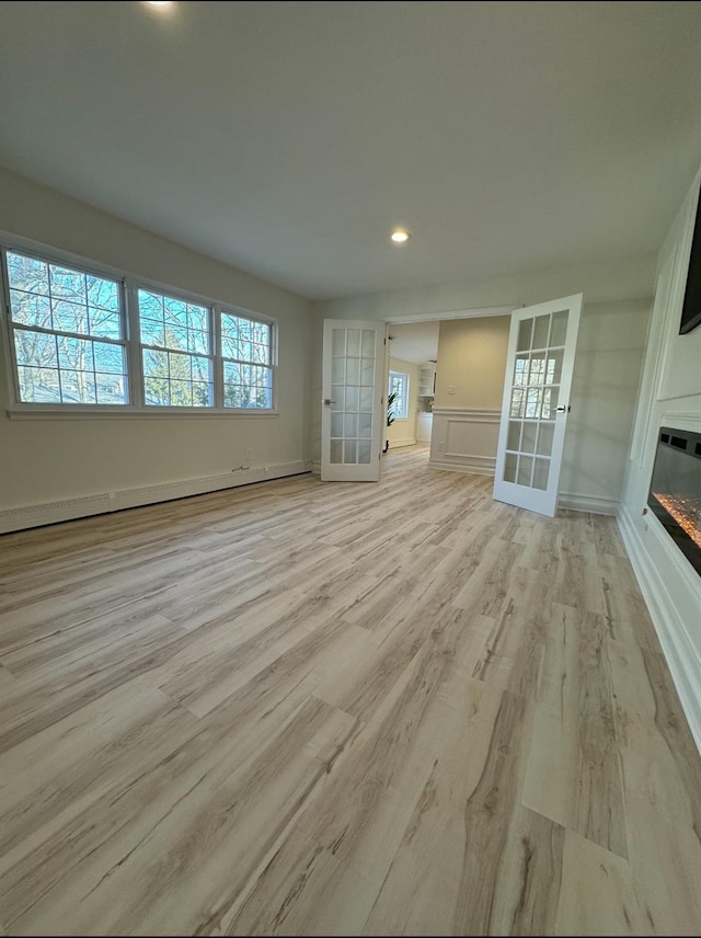 unfurnished living room with light wood finished floors, a baseboard radiator, french doors, and a glass covered fireplace