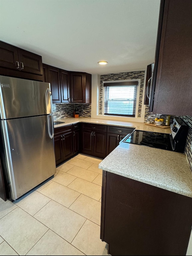 kitchen featuring dark brown cabinetry, light tile patterned floors, decorative backsplash, appliances with stainless steel finishes, and light stone countertops