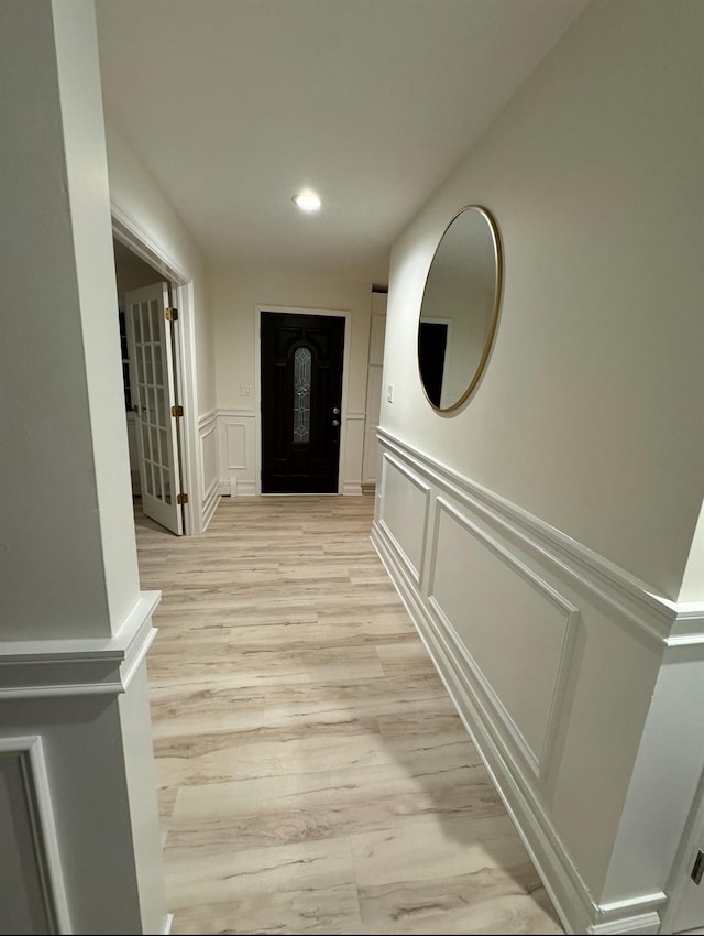 hallway with light wood-style floors, recessed lighting, wainscoting, and a decorative wall