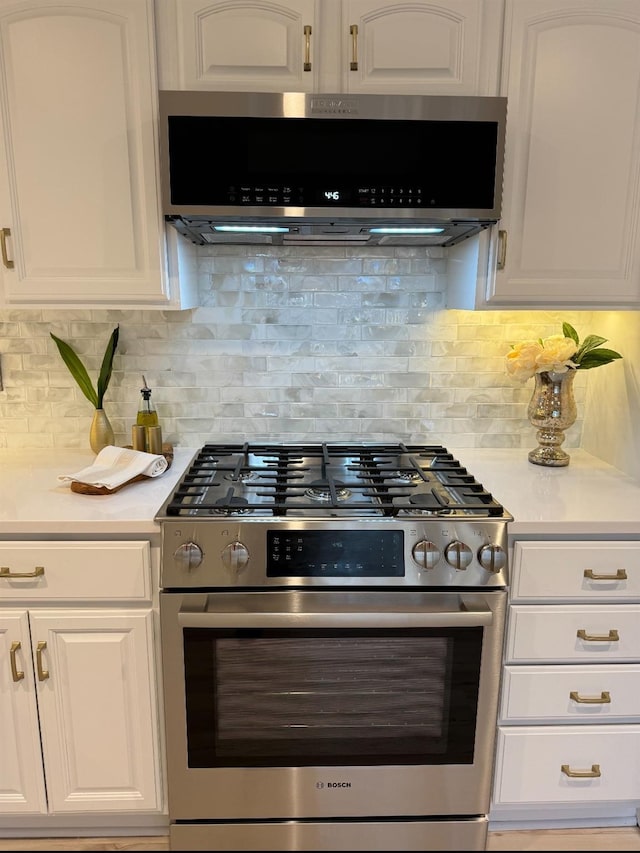 kitchen with stainless steel gas range oven, white cabinetry, light countertops, backsplash, and range hood