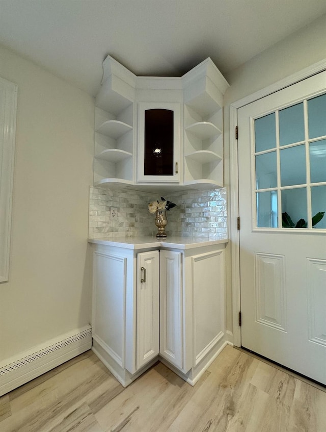 bar with light wood-style floors, a baseboard heating unit, and backsplash