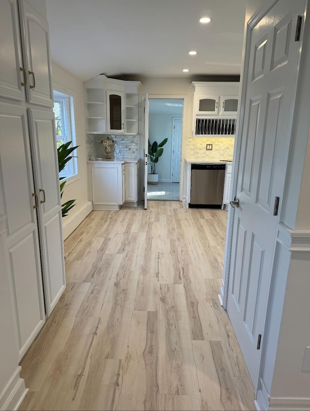 kitchen with light wood finished floors, open shelves, backsplash, stainless steel dishwasher, and white cabinets