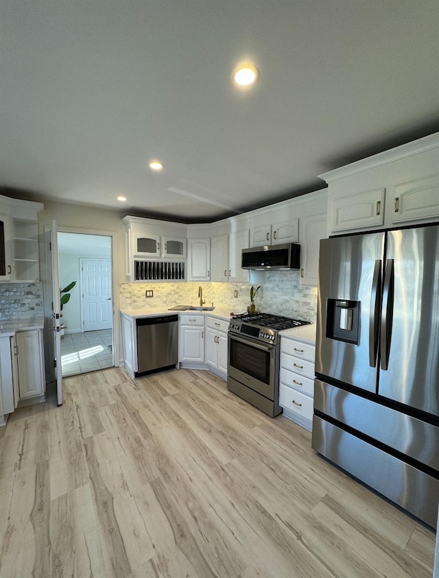 kitchen with light wood finished floors, decorative backsplash, appliances with stainless steel finishes, light countertops, and a sink