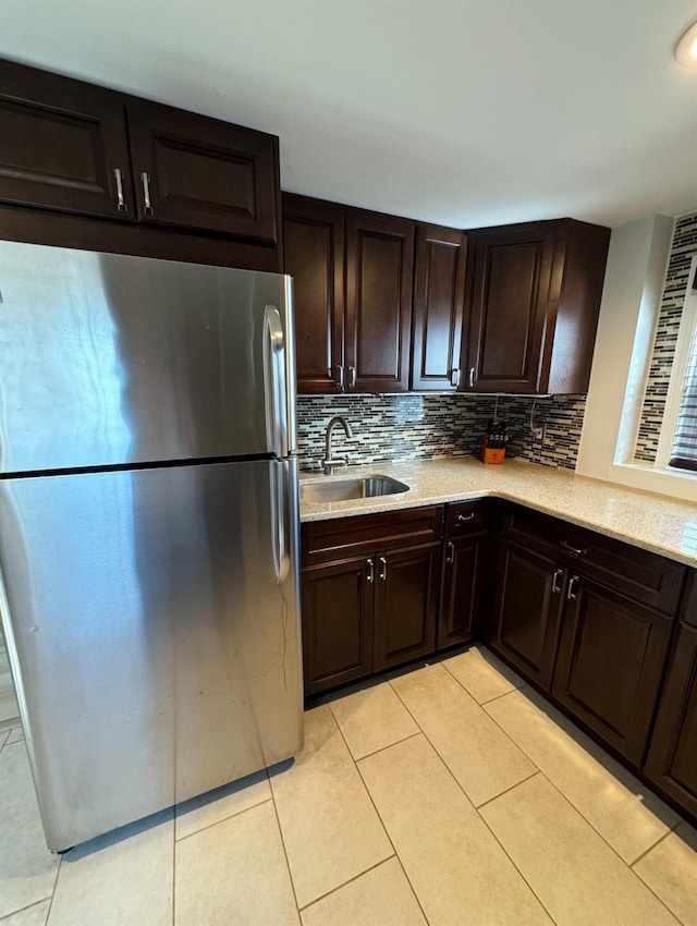 kitchen with light tile patterned floors, backsplash, freestanding refrigerator, a sink, and dark brown cabinetry