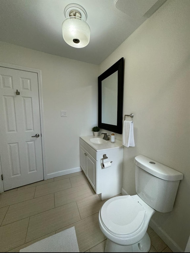 half bathroom featuring toilet, baseboards, and vanity