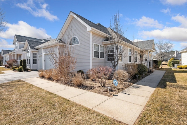 view of side of property with a residential view, concrete driveway, a lawn, and an attached garage