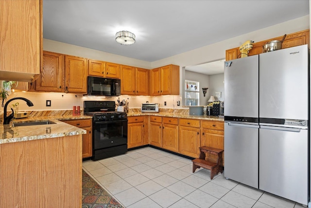 kitchen with light tile patterned floors, a sink, light stone countertops, black appliances, and tasteful backsplash